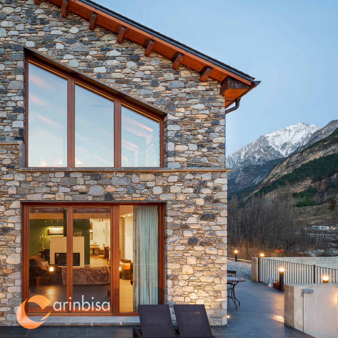 Fachada de piedra y madera con grandes huecos abiertos al paisaje